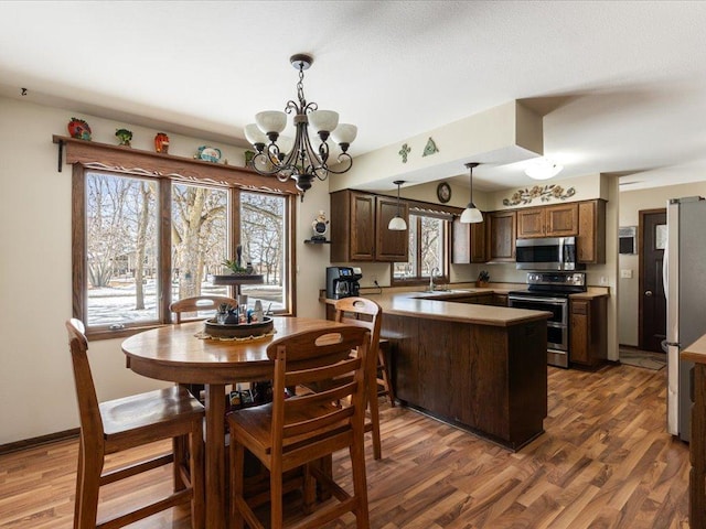 kitchen with pendant lighting, light countertops, appliances with stainless steel finishes, wood finished floors, and a peninsula