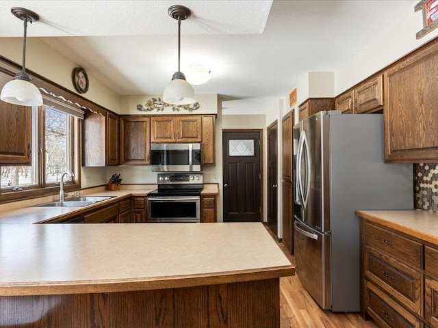 kitchen featuring pendant lighting, light countertops, light wood-style flooring, appliances with stainless steel finishes, and a sink