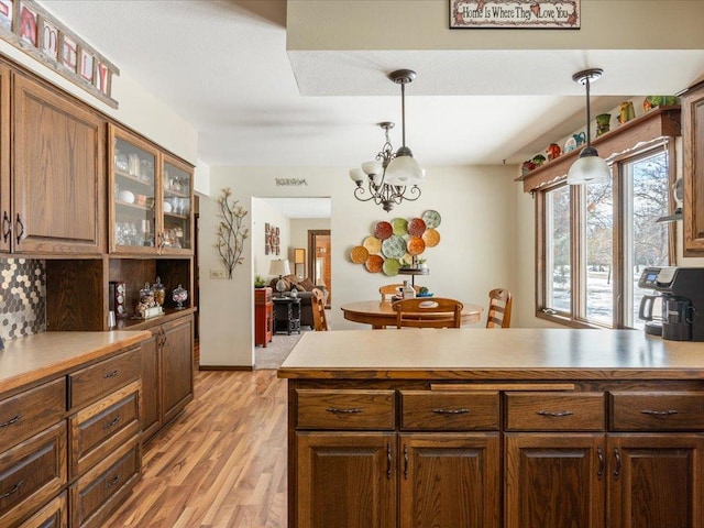 kitchen with light wood-type flooring, glass insert cabinets, light countertops, and decorative light fixtures