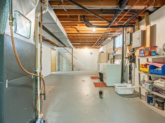 unfinished basement featuring concrete block wall, heating unit, washing machine and dryer, electric panel, and stairs