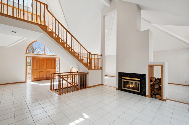unfurnished living room featuring high vaulted ceiling, stairway, tile patterned floors, a fireplace, and baseboards