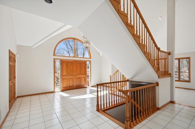 entryway with light tile patterned flooring, baseboards, a chandelier, stairs, and high vaulted ceiling