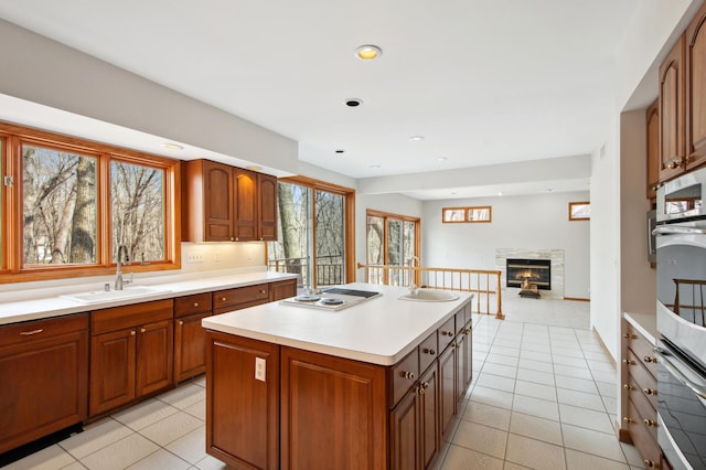 kitchen with light countertops, a glass covered fireplace, a kitchen island, and a sink