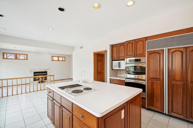 kitchen with a stone fireplace, brown cabinetry, white appliances, light tile patterned floors, and light countertops