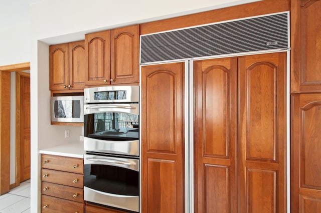 kitchen featuring built in appliances, brown cabinetry, light tile patterned flooring, and light countertops