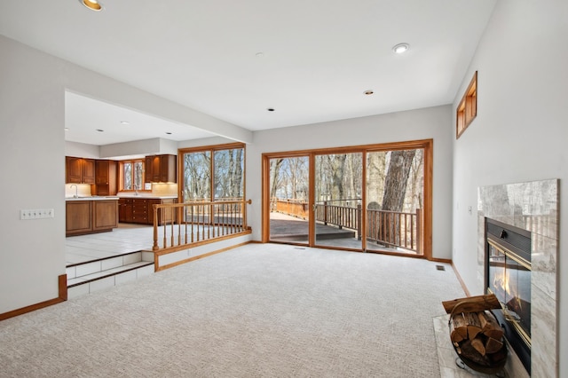 unfurnished living room with a tile fireplace, baseboards, recessed lighting, and light colored carpet