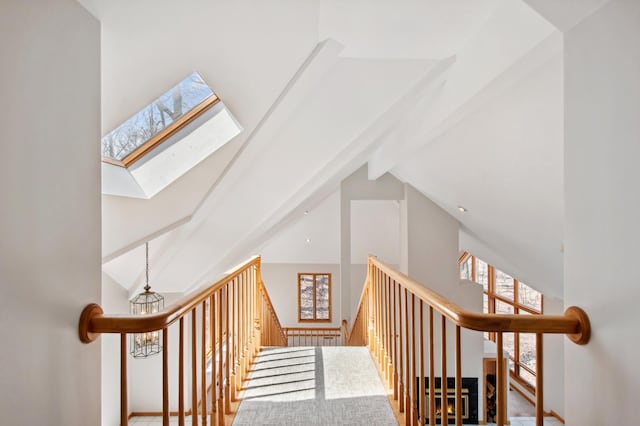 stairway with a skylight, beam ceiling, and high vaulted ceiling