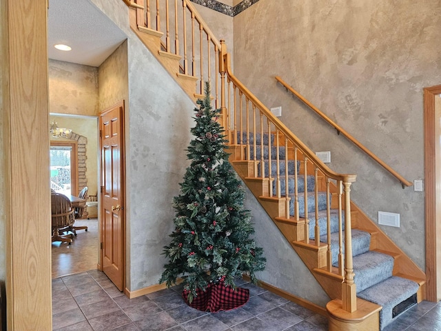 stairway featuring tile patterned flooring, a notable chandelier, a towering ceiling, and a textured ceiling