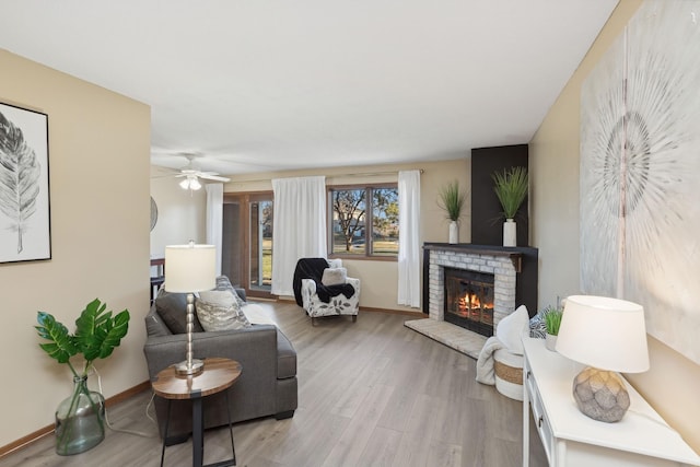 living room featuring a brick fireplace, light hardwood / wood-style flooring, and ceiling fan