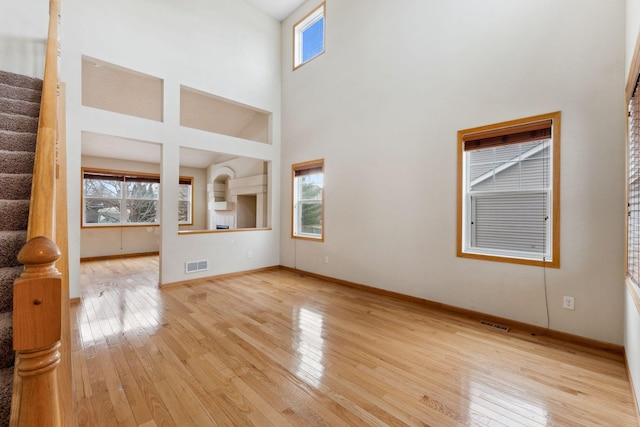 unfurnished living room featuring a towering ceiling, a healthy amount of sunlight, and light wood-type flooring