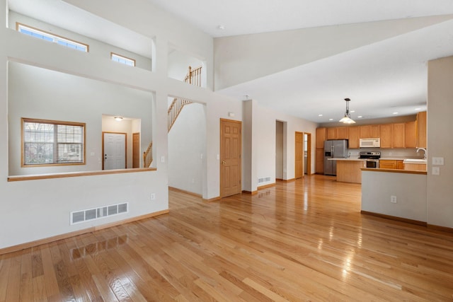 unfurnished living room featuring light hardwood / wood-style floors, high vaulted ceiling, and sink