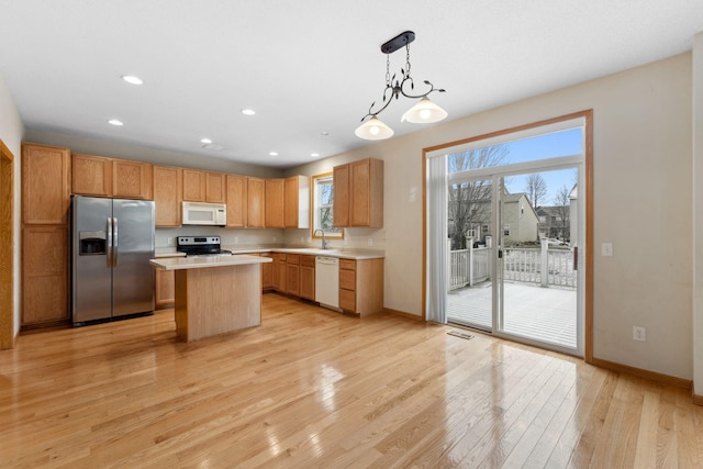 kitchen featuring appliances with stainless steel finishes, light wood-type flooring, sink, a kitchen island, and hanging light fixtures