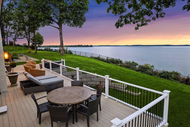 wooden deck featuring outdoor dining area, a water view, and a lawn