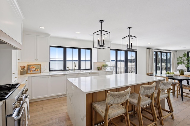 kitchen featuring white cabinetry, a kitchen island, light wood finished floors, a sink, and high end stainless steel range oven