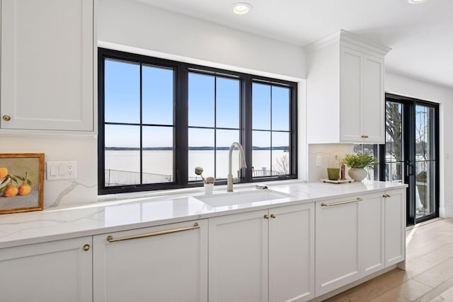 kitchen featuring light stone countertops, white cabinetry, a water view, and a sink