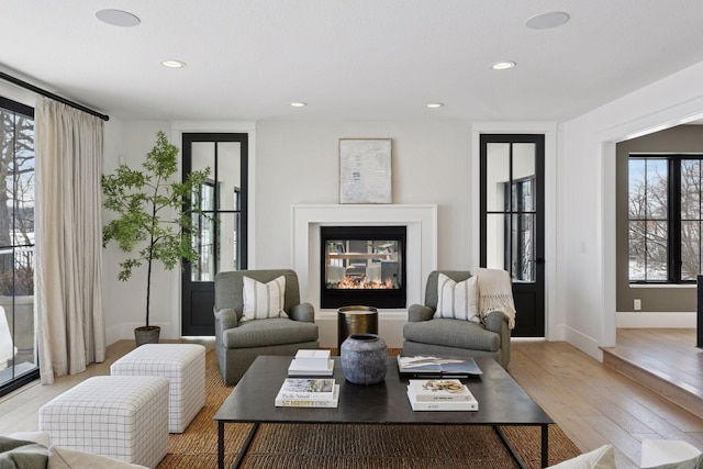 living area with recessed lighting, light wood-type flooring, baseboards, and a glass covered fireplace