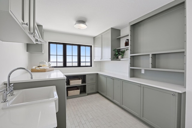 kitchen featuring a sink, open shelves, light countertops, and gray cabinetry