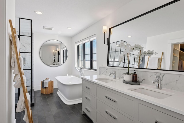 full bath featuring a sink, decorative backsplash, double vanity, and a freestanding tub