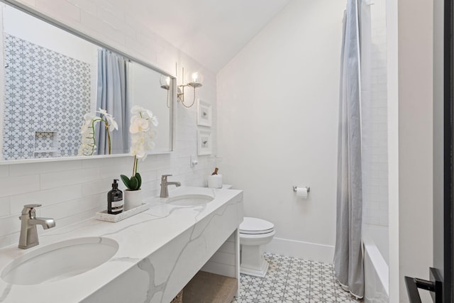 bathroom featuring double vanity, vaulted ceiling, toilet, and a sink