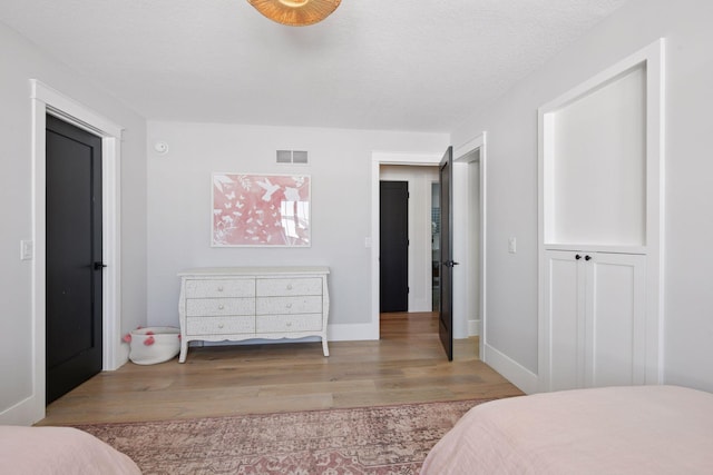 bedroom with baseboards, wood finished floors, visible vents, and a textured ceiling