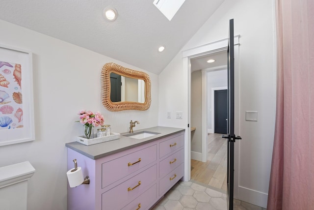 full bath with tile patterned flooring, toilet, vanity, vaulted ceiling with skylight, and a textured ceiling