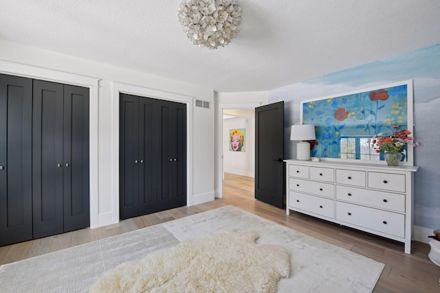 bedroom with visible vents, two closets, baseboards, wood finished floors, and a textured ceiling