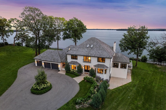 view of front of house with a front lawn, a water view, driveway, and a chimney