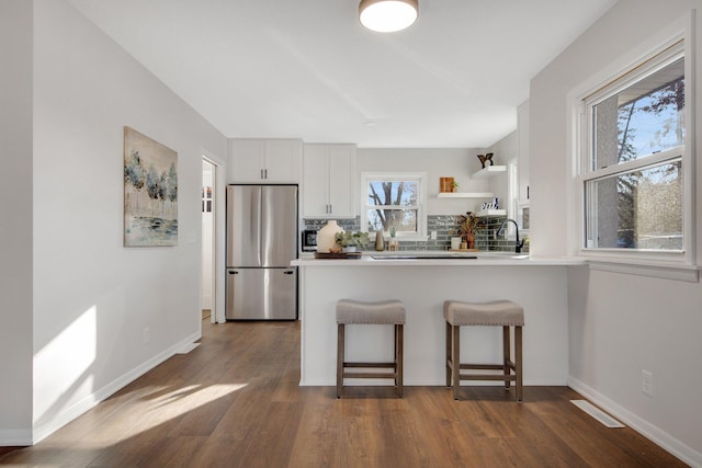 kitchen featuring a breakfast bar, white cabinets, tasteful backsplash, dark hardwood / wood-style flooring, and stainless steel refrigerator