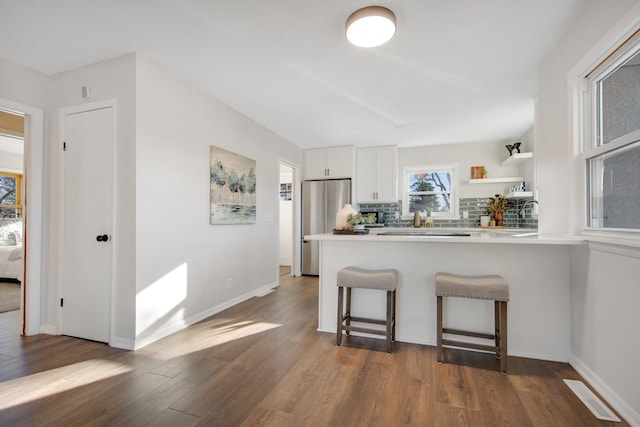 kitchen featuring dark hardwood / wood-style flooring, tasteful backsplash, white cabinetry, and stainless steel refrigerator