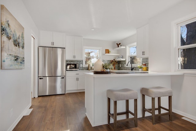 kitchen with appliances with stainless steel finishes, backsplash, dark hardwood / wood-style flooring, a breakfast bar, and white cabinets