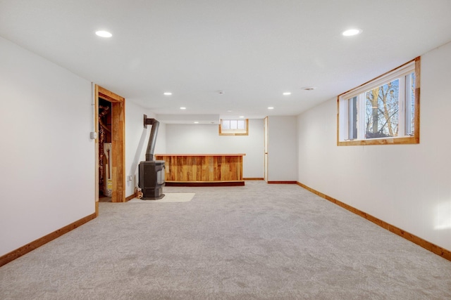 basement featuring light colored carpet, a wood stove, and a wealth of natural light