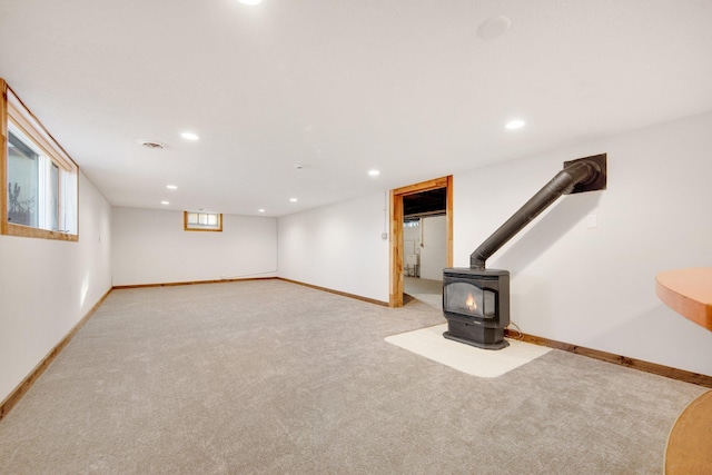 basement featuring light colored carpet and a wood stove