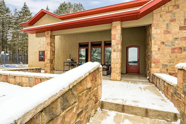 snow covered property entrance with stone siding and covered porch