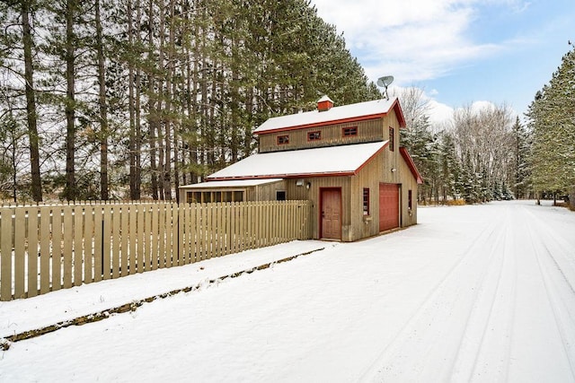 snow covered structure with an outbuilding and fence