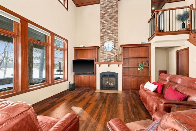 living area featuring a large fireplace, visible vents, dark wood-style flooring, and a towering ceiling