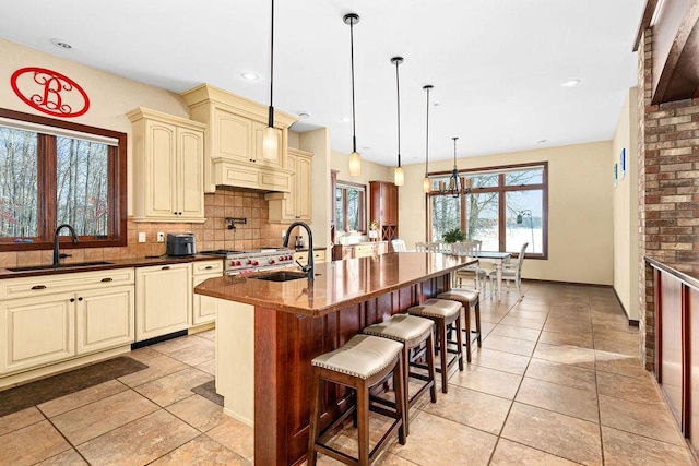 kitchen featuring an island with sink, cream cabinets, decorative backsplash, and a sink