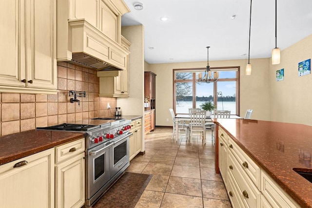 kitchen featuring tasteful backsplash, dark stone countertops, hanging light fixtures, cream cabinets, and double oven range