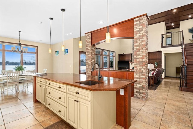 kitchen with cream cabinetry, open floor plan, a sink, an island with sink, and dark stone counters