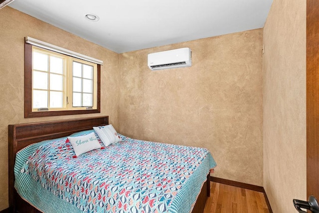 bedroom with an AC wall unit and wood finished floors