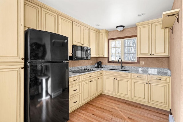 kitchen with black appliances, cream cabinetry, light wood-type flooring, and a sink