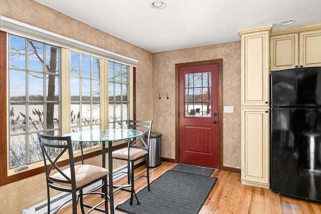 interior space featuring baseboard heating, baseboards, a water view, and light wood finished floors