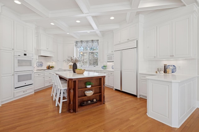 kitchen with white appliances, a breakfast bar, a center island, and white cabinets