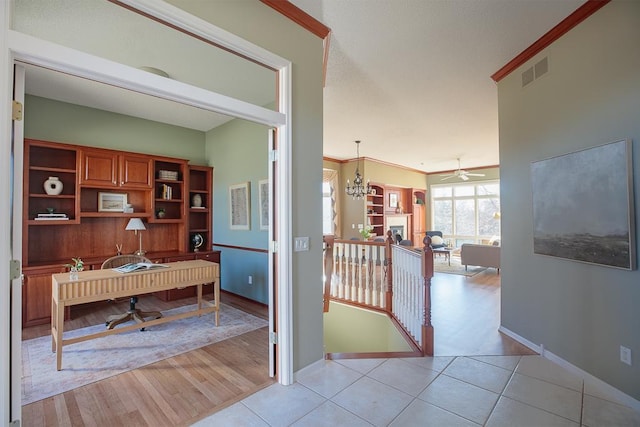 office area with crown molding, visible vents, light wood-type flooring, baseboards, and ceiling fan with notable chandelier