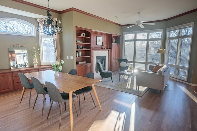 dining space featuring a notable chandelier, light wood-style flooring, crown molding, and a glass covered fireplace