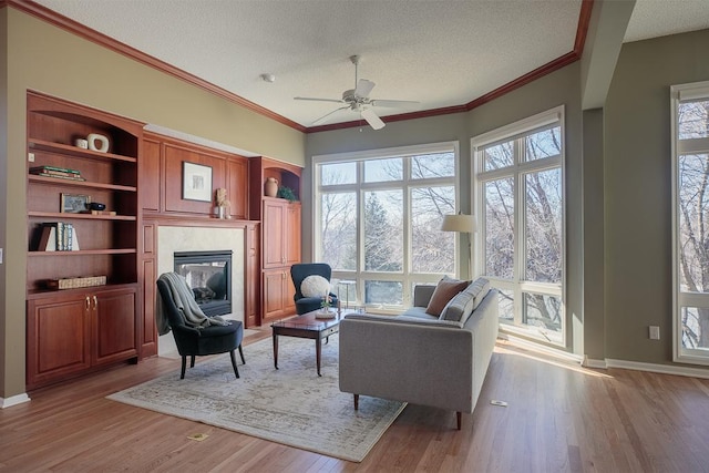 living area with light wood-type flooring, ornamental molding, a textured ceiling, and a glass covered fireplace