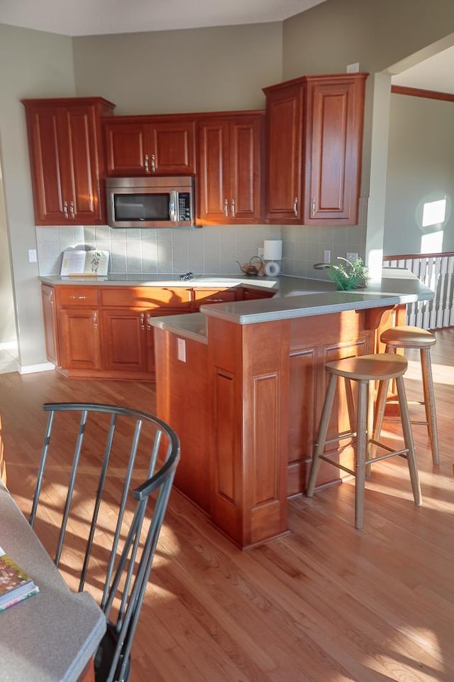 kitchen featuring light wood finished floors, stainless steel microwave, a kitchen breakfast bar, a peninsula, and backsplash