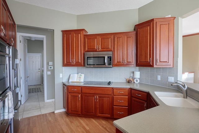 kitchen featuring appliances with stainless steel finishes, light wood-type flooring, a sink, and tasteful backsplash