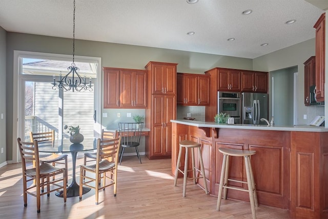 kitchen featuring light wood-style flooring, stainless steel appliances, a peninsula, a kitchen breakfast bar, and brown cabinets