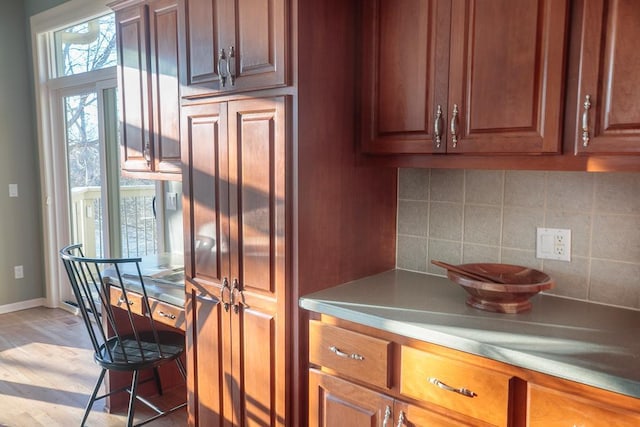 kitchen with brown cabinets, light wood finished floors, baseboards, and decorative backsplash