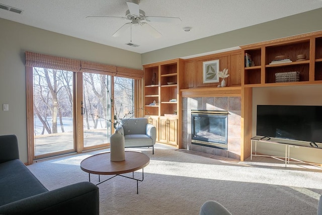 carpeted living room with ceiling fan, visible vents, and a tile fireplace